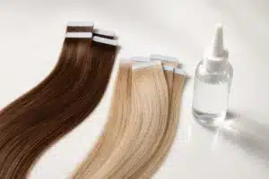 Brown and blonde tape-in tabs beside an unbranded clear remover bottle on a clean studio surface.