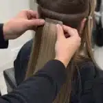 Stylist applying tape in hair extensions for a maintenance guide