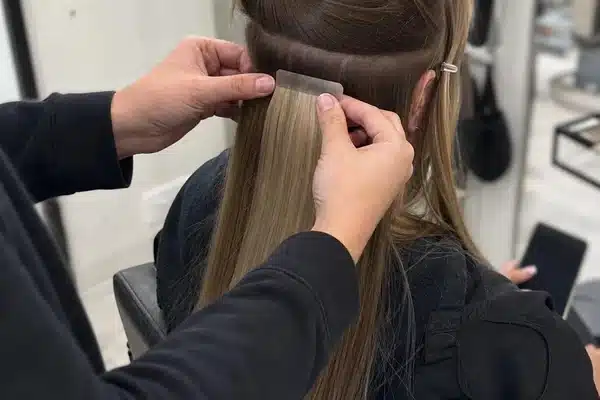Stylist applying tape in hair extensions for a maintenance guide