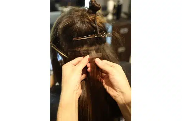 Stylist preparing tape in hair extensions during a salon installation