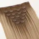 Warm-blonde clip-in human hair extension set with visible pressure clips on the wefts.