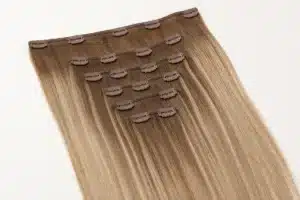 Warm-blonde clip-in human hair extension set with visible pressure clips on the wefts.