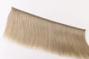 Ash-blonde human hair weft with a visible stitched seam for wholesale sample testing.