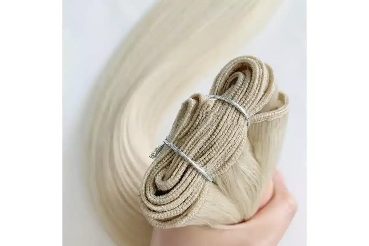 Light-blonde machine weft hair rolled to show a dense stitched seam.