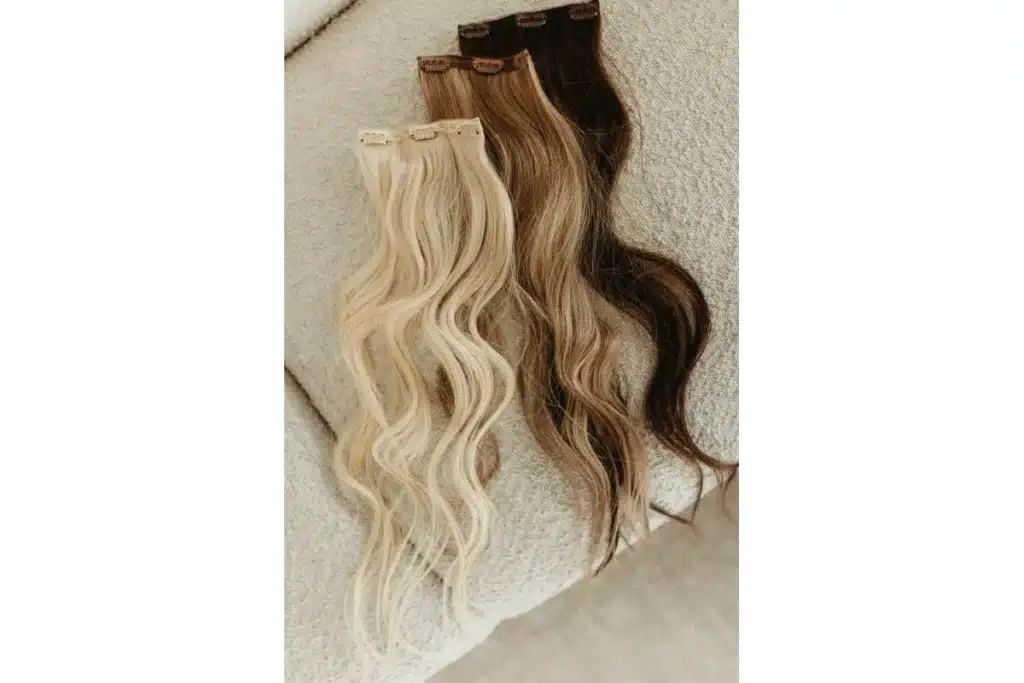 Blonde and brunette wavy clip in extension pieces arranged on a neutral surface.