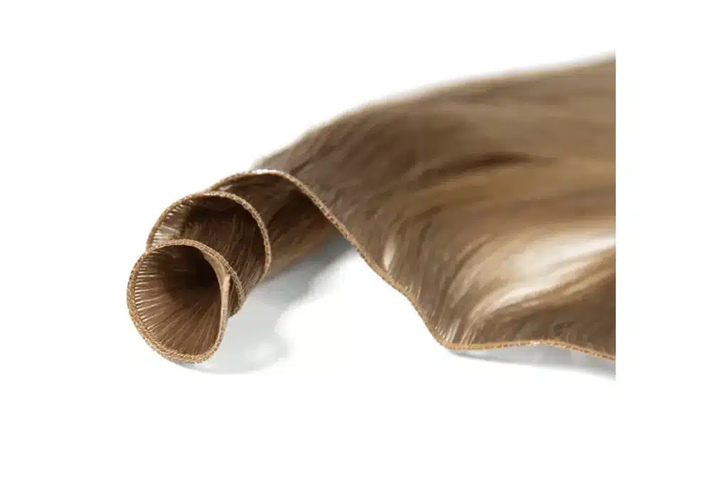A light brown hair weft partly rolled to show its narrow attachment edge and flowing strands.