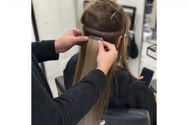 Stylist placing a tape-in piece beneath a clean parting during fitting.